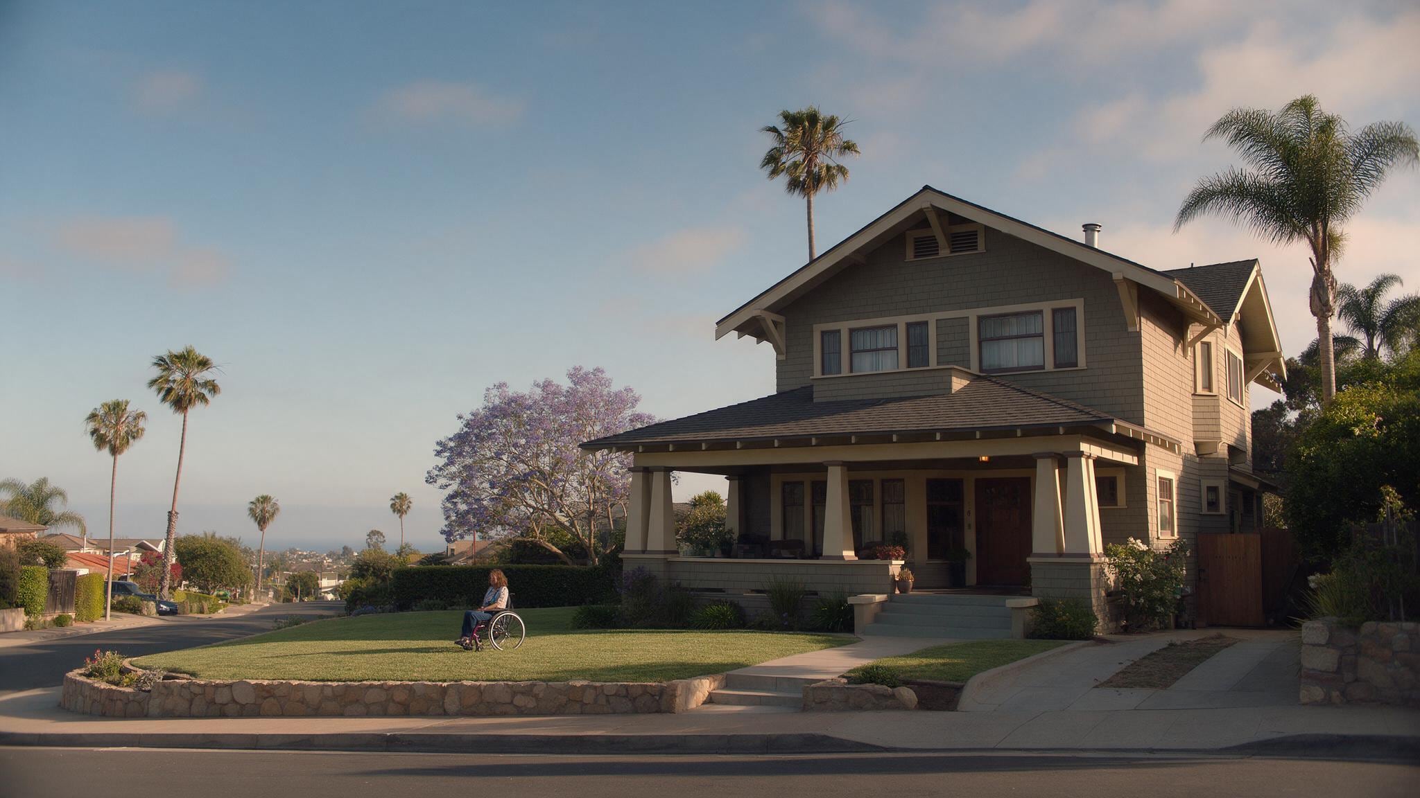 Two-story residential home with front porch, palm trees, and flowering jacaranda tree in warm afternoon sunlight.